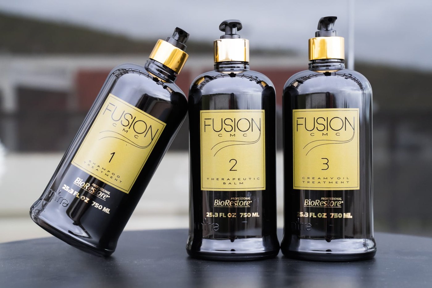 Três frascos pretos e dourados da linha Fusion CMC BioRestore: shampoo, balm terapêutico e creamy oil