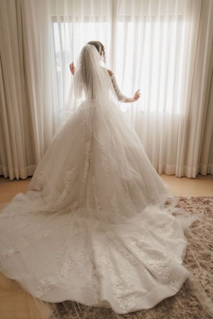Noiva de costas, olhando pela janela, com vestido e véu longos