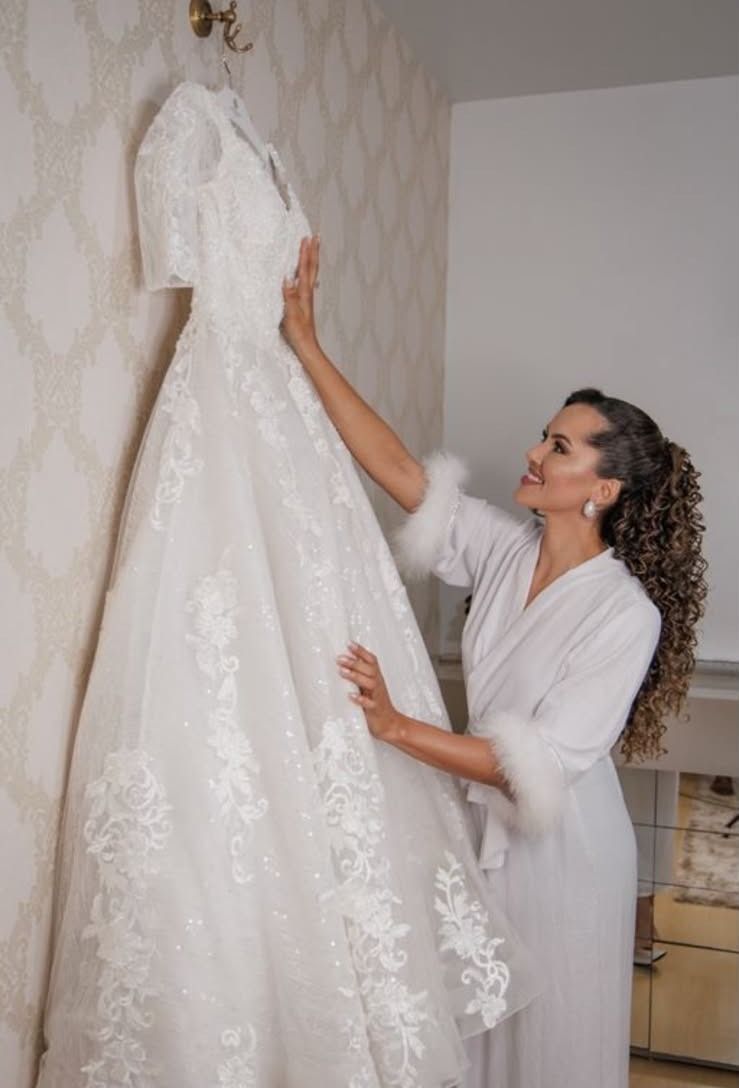 Jaqueline ajeitando o vestido de noiva pendurado